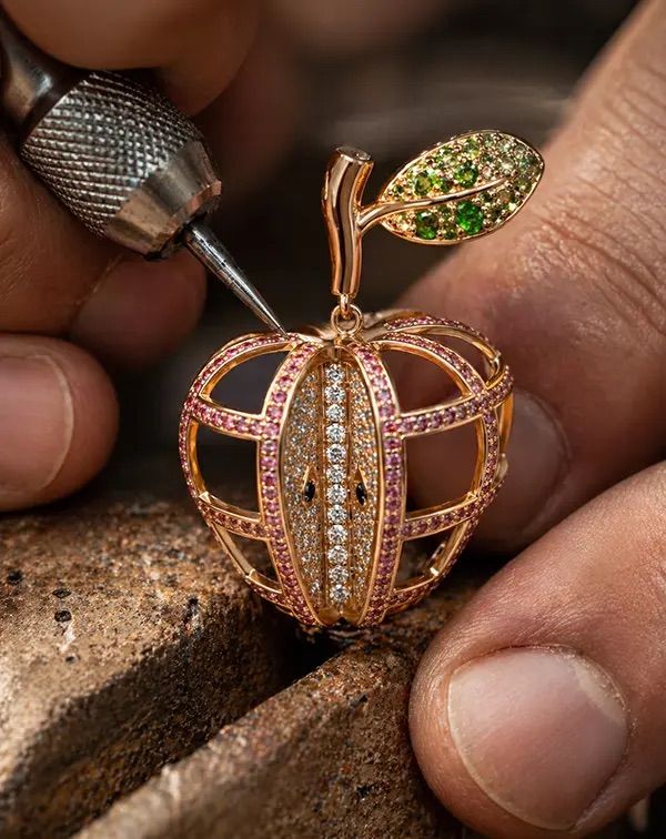 Artisan sertissant un pendentif pomme en or et pierres