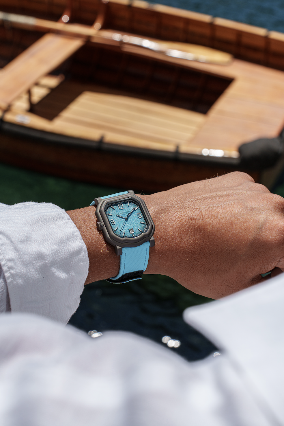 Montre bleue au poignet devant une barque en bois