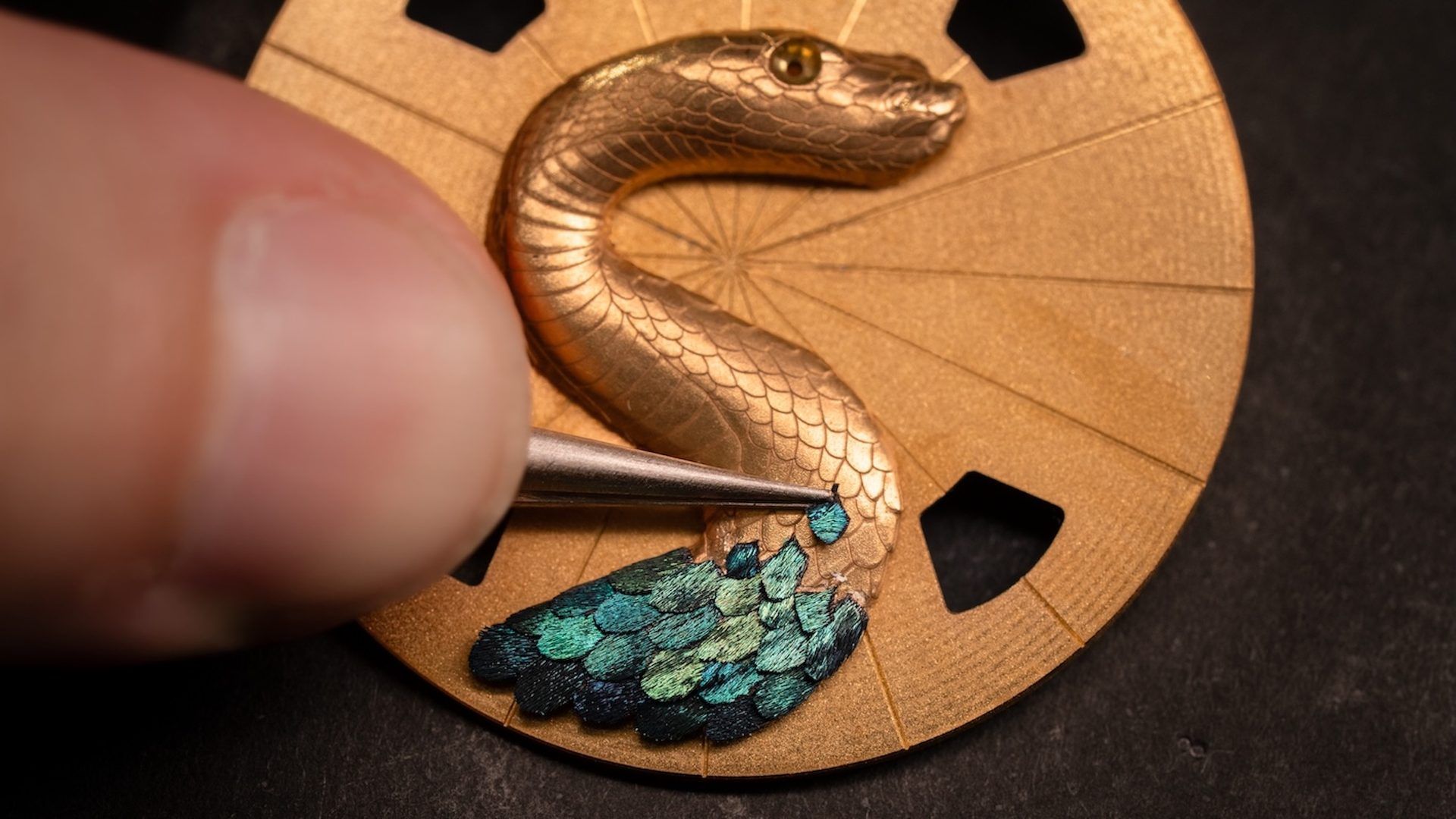 Brodeuse réalisant un serpent sur support circulaire doré